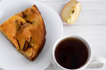 a white Cup with tea next to a piece of delicious ruddy Apple pie on a white plate