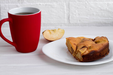 a mug of red tea or coffee next to a piece of Apple pie on a white plate