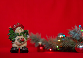Closeup of Christmas composition of snowman and blurred fir branch with Christmas tree balls on red background. Merry Christmas card. Winter holiday xmas theme. Happy New Year. Space for text.