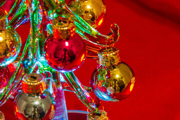 Ornaments of a mini Christmas Tree made of glass illuminated and set against a red background viewed from the side.