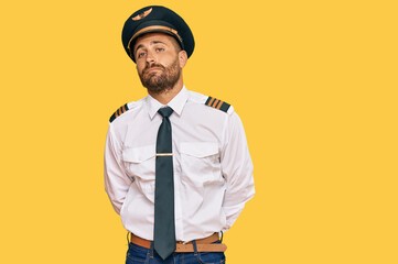 Handsome man with beard wearing airplane pilot uniform relaxed with serious expression on face....