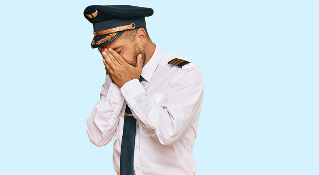 Handsome man with beard wearing airplane pilot uniform with sad expression covering face with hands while crying. depression concept.