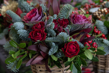 Beautiful flower arrangement of red roses, Brassica oleracea, natural spruce branches for winter festive indoor decor.