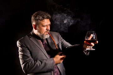 Solid confident bearded man in suit with glass of whisky smoking pipe