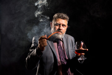 Solid confident bearded man in suit with glass of whisky smoking pipe