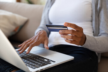 Crop close up of African American female client or customer shopping online on computer with credit card. Biracial woman make payment or purchase on web, use internet banking secure system.
