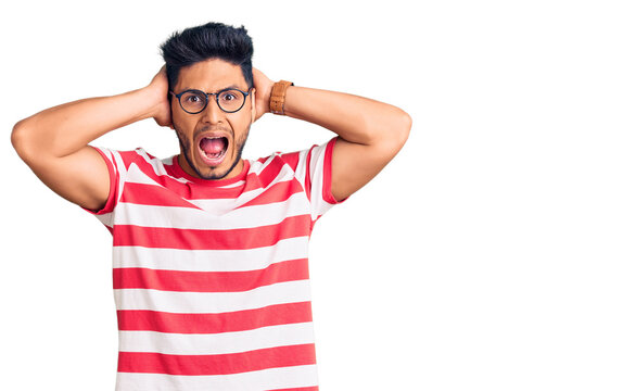 Handsome latin american young man wearing casual clothes and glasses crazy and scared with hands on head, afraid and surprised of shock with open mouth