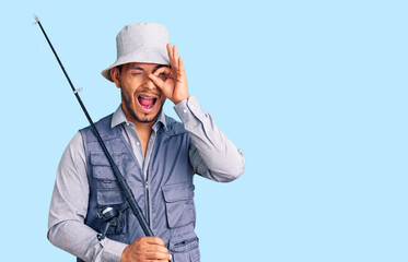 Handsome latin american young man wearing fisherman equipment smiling happy doing ok sign with hand on eye looking through fingers