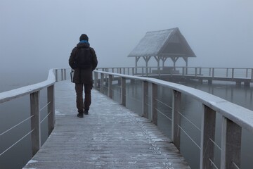 back view of a man walking along a wooden jetty in fog in winter