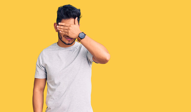 Handsome latin american young man wearing casual tshirt smiling and laughing with hand on face covering eyes for surprise. blind concept.