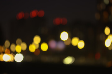Fototapeta premium The facade of the apartment building, light in the windows in the evening, blurred houses in the big city and bright colorful abstract lights. 