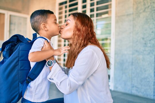 Adorable latin student boy and mom at school. Mother preparing kid putting up backpack. and kissing.