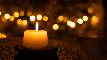 A candle burns against a blurred golden bokeh background. Close-up, blurred background. Festive New Year background.