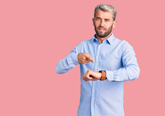 Young handsome blond man wearing elegant shirt in hurry pointing to watch time, impatience, upset and angry for deadline delay