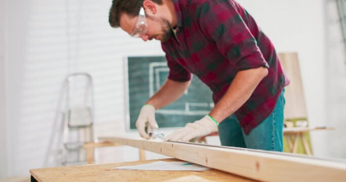 Close up of a hardworking professional carpenter holding a ruler and pencil while making a board center in a carpentry workshop. A bearded DIY enthusiast measures wood.