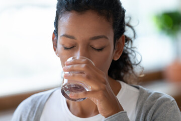 Crop close up of dehydrated millennial African American woman drink clean clear still mineral water...