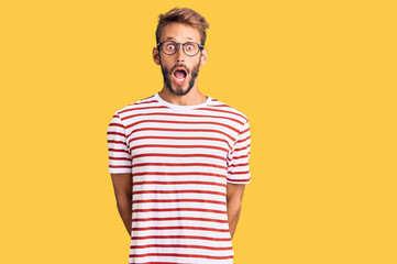 Handsome blond man with beard wearing casual clothes and glasses afraid and shocked with surprise...