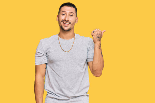 Handsome man with tattoos wearing 90s style smiling with happy face looking and pointing to the side with thumb up.