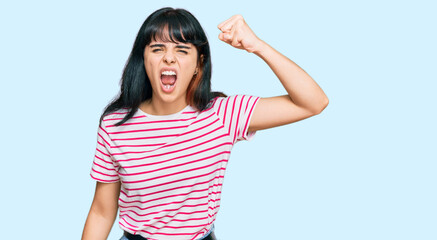 Obraz na płótnie Canvas Young hispanic girl wearing casual clothes angry and mad raising fist frustrated and furious while shouting with anger. rage and aggressive concept.