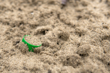Fototapeta na wymiar A green cork from a plastic bottle lies in the sand. Environmental pollution with plastic waste. Nature protection concept. Save ecology for future generations.