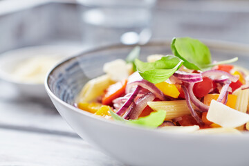 Penne pasta with yellow and red pepper, hard cheese and fresh basil. Bright background. Close up.	