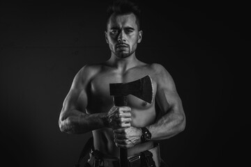 Fototapeta na wymiar young handsome adult, muscular firefighter in uniform holding an ax fire equipment, pensively looking straight, isolated on a dark background. Low key. Protection concept. Black and white photo