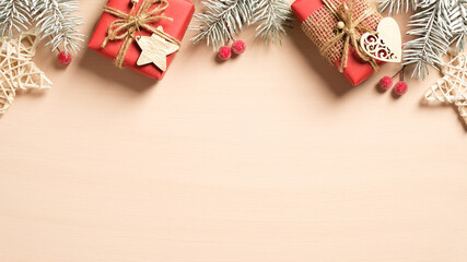 Christmas frame top border made of pine tree branches with red berries, handmade gift boxes and Christmas decorations on pastel beige background. Flat lay, top view. Xmas banner mockup with copy space