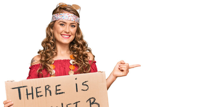 Young blonde girl wearing hippie style holding there is no planet b banner smiling happy pointing with hand and finger to the side
