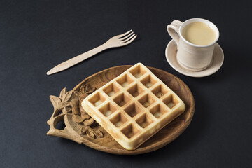 Homemade waffle on a wooden plate with coffe cup on a dark ambient backdrop.