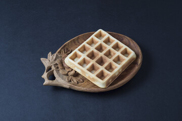 Homemade waffle on a wooden plate with coffe cup on a dark ambient backdrop.