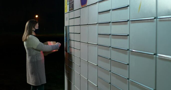 Woman is Skanning Bar Code in Parcel Locker to Send, Return or Deliver Box at Night. Modern Shipping and Internet Shopping Concept. Customer Uses in Self-service Contactless Locker. 4K Medium Shot