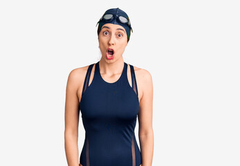 Young beautiful hispanic woman wearing swimwear and swimmer glasses afraid and shocked with surprise expression, fear and excited face.