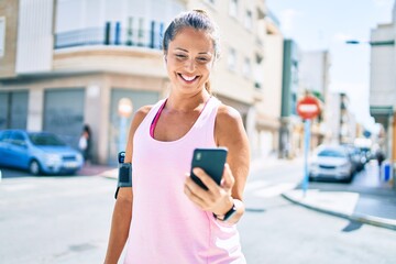 Middle age sportswoman smiling happy using smartphone at the city