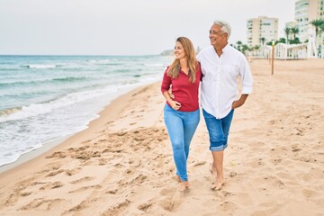 Middle age hispanic couple smiling happy walking at the beach.