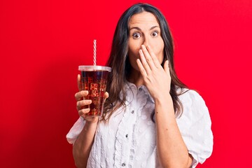 Beautiful brunette woman drinking cola refreshment beverage using straw over red background...