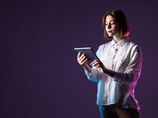 Student girl with a tablet in her hands. Online learning. A young girl is using a tablet PC. The girl stands and holds a digital tablet on a plum background.