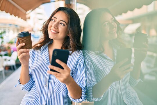 Young hispanic businesswoman using smartphone and drinking take away coffee at the city.