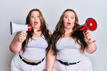 Plus size caucasian sisters woman shouting through megaphone afraid and shocked with surprise and amazed expression, fear and excited face.