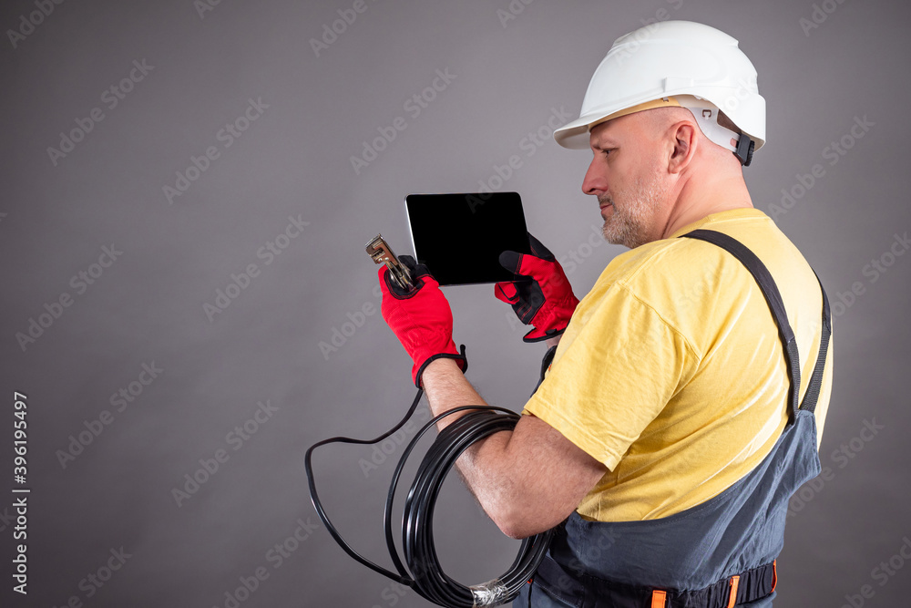 Poster electrician on a gray background. electrician in a work uniform looks at information in an electroni