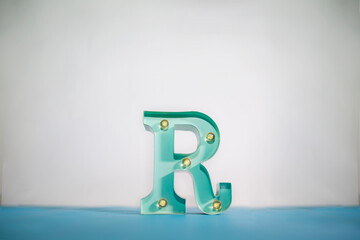 Letter R turquoise color with lights, white and light blue background