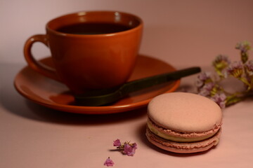 Obraz na płótnie Canvas Cup of coffee with chocolate spoon and pink macaroon on a pink background with flowers