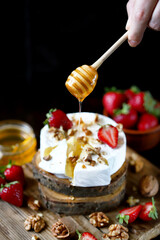 Camembert cheese with strawberries and nuts. A honey stick pours honey on a Camembert. Healthy dessert. An exquisite beautiful dessert.