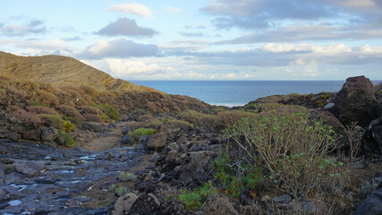 Hike path between volcanic rocks leading to the ocean in El Medano, Tenerife, Canary Islands, Spain     