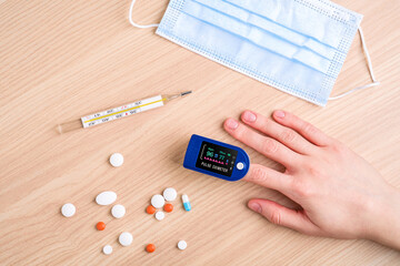 Person using pulse oximeter device near to pills, thermometer and medical mask, healthcare...