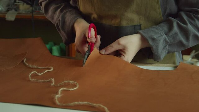 A tanner in a work apron cuts out an element of a women's bag made of genuine leather in the workshop.