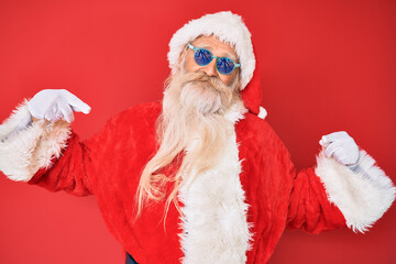 Old senior man wearing santa claus costume and sunglasses looking confident with smile on face, pointing oneself with fingers proud and happy.