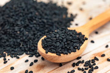 Black cumin seeds on wooden spoon on wooden background