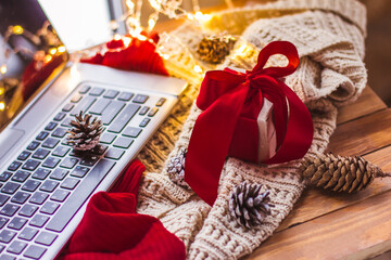 Gift with a red bow and laptop Christmas cones and a light knitted scarf Christmas online shopping