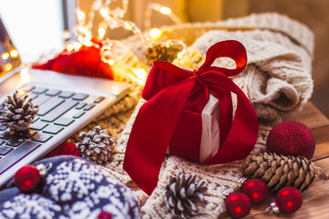 Gift with a red bow and laptop Christmas cones and a light knitted scarf Christmas online shopping