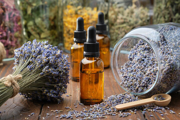 Dropper bottle of lavender essential oil, glass jar of dry lavender flowers, bunches of dry lavender. Jars of different dry medicinal herbs on background. Alternative medicine.